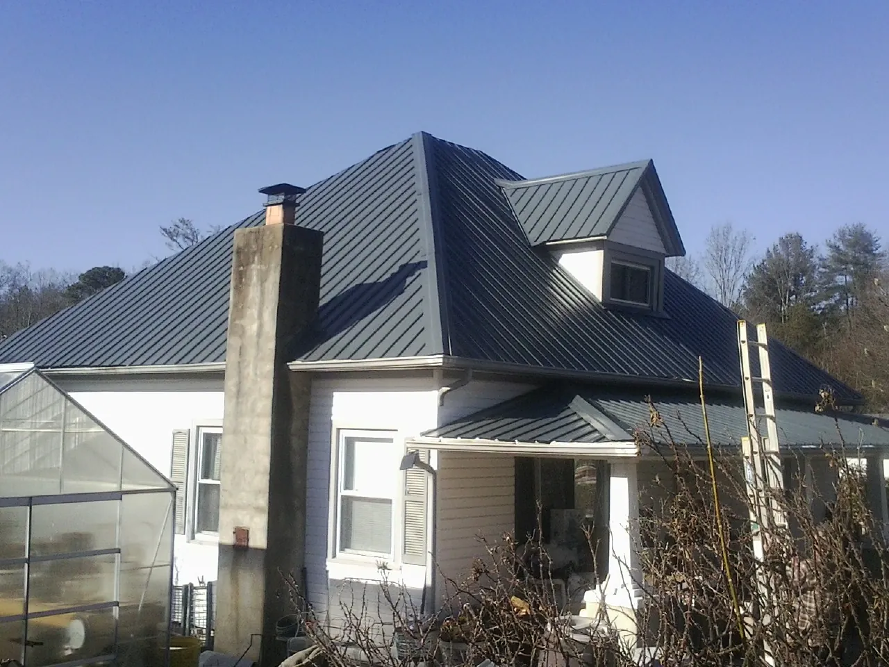 Dark blue standing seam metal roof on a white farmhouse with dormer — Slate & Tile Roof Repair by Roofing Brothers in Okolona