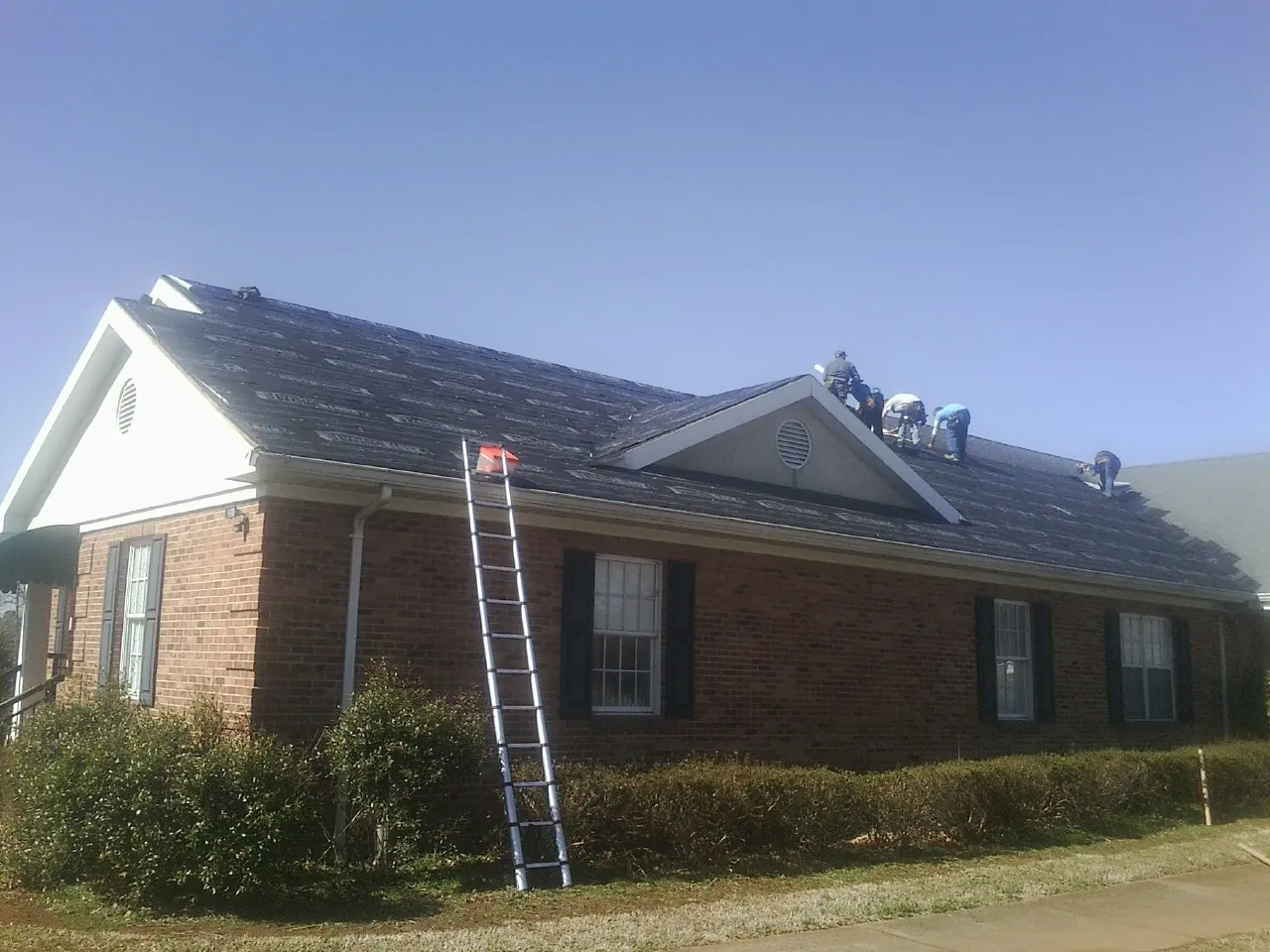 Crew tearing shingles off a brick ranch roof with a ladder set — Metal Roof Repair work by our crew in Okolona