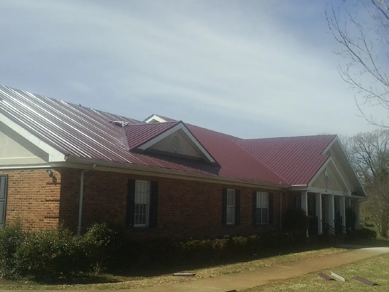 Red metal roof with gabled entries on a long brick building, from a Hail Damage Roof Repair job in Okolona