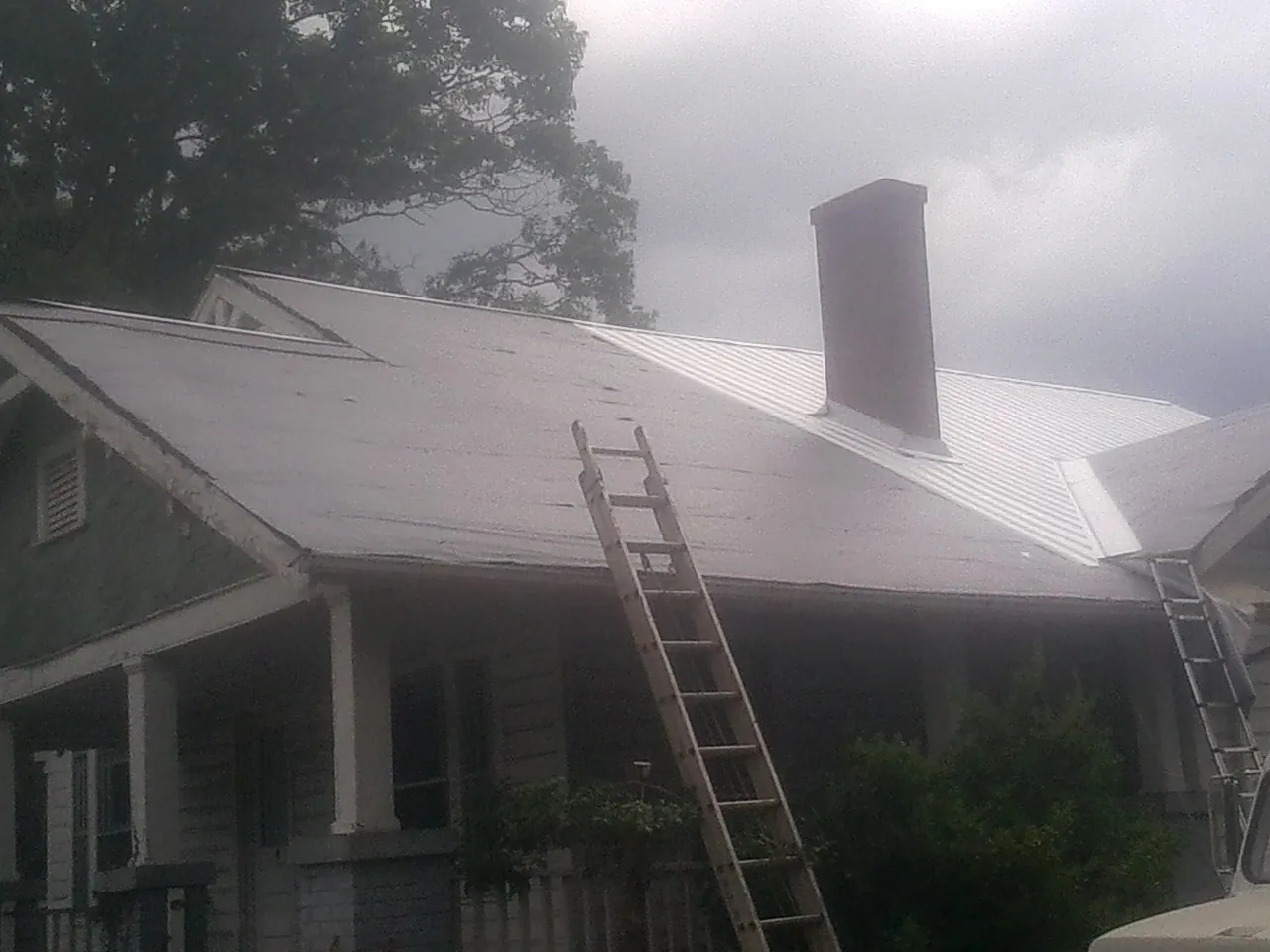 Ladders against a metal roof on an older home with a brick chimney in Okolona