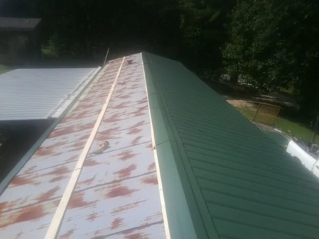Old rusted panels beside newly installed green metal roofing — Wind Damage Roof Repair by Roofing Brothers in Okolona