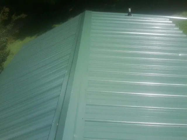 New green metal panels meeting at the ridge of a roof — Flat Roof Repair work by our crew in Okolona