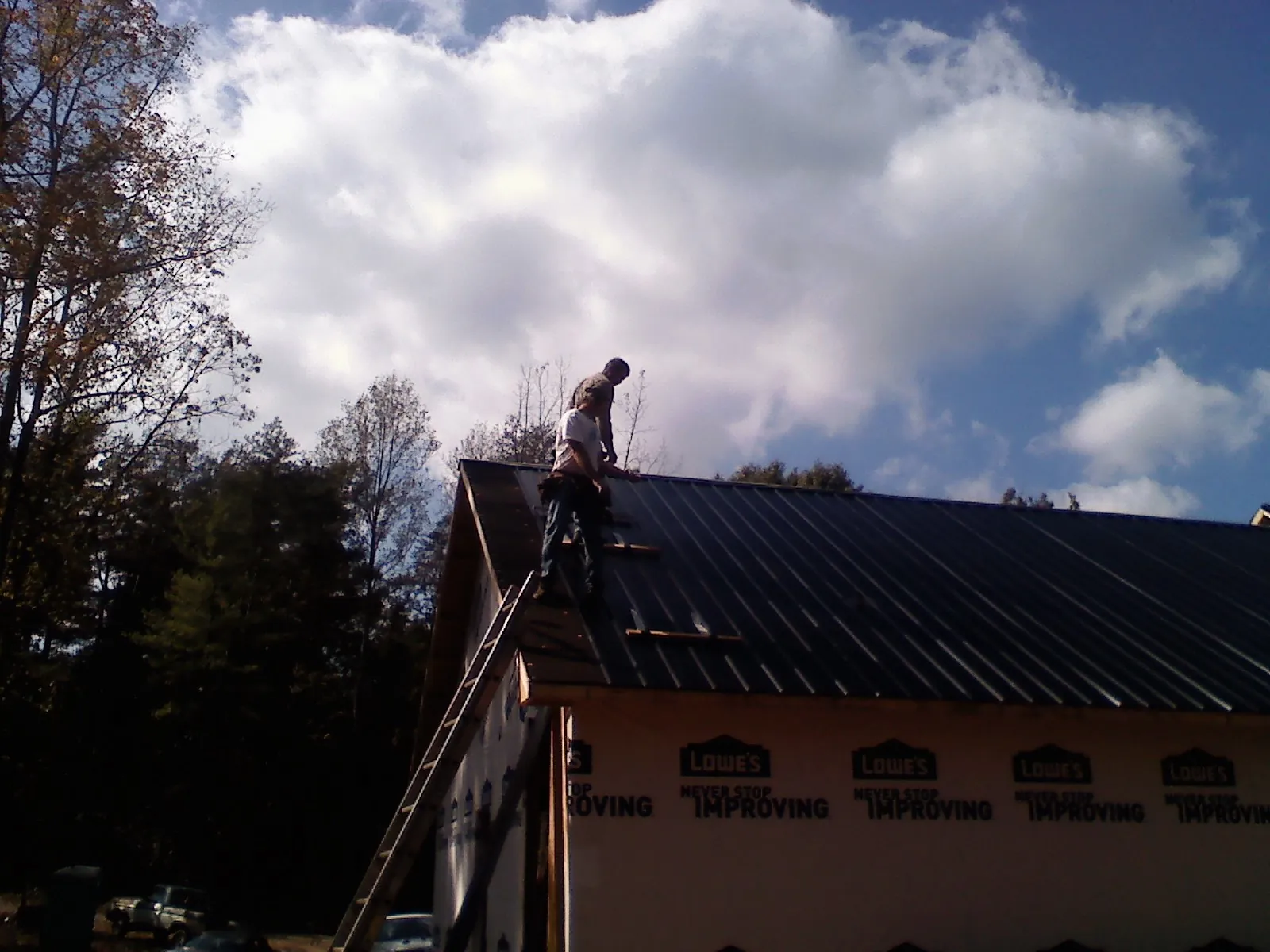 Roofer fastening dark metal panels high against a cloudy sky, from a Roof Inspection job in Okolona