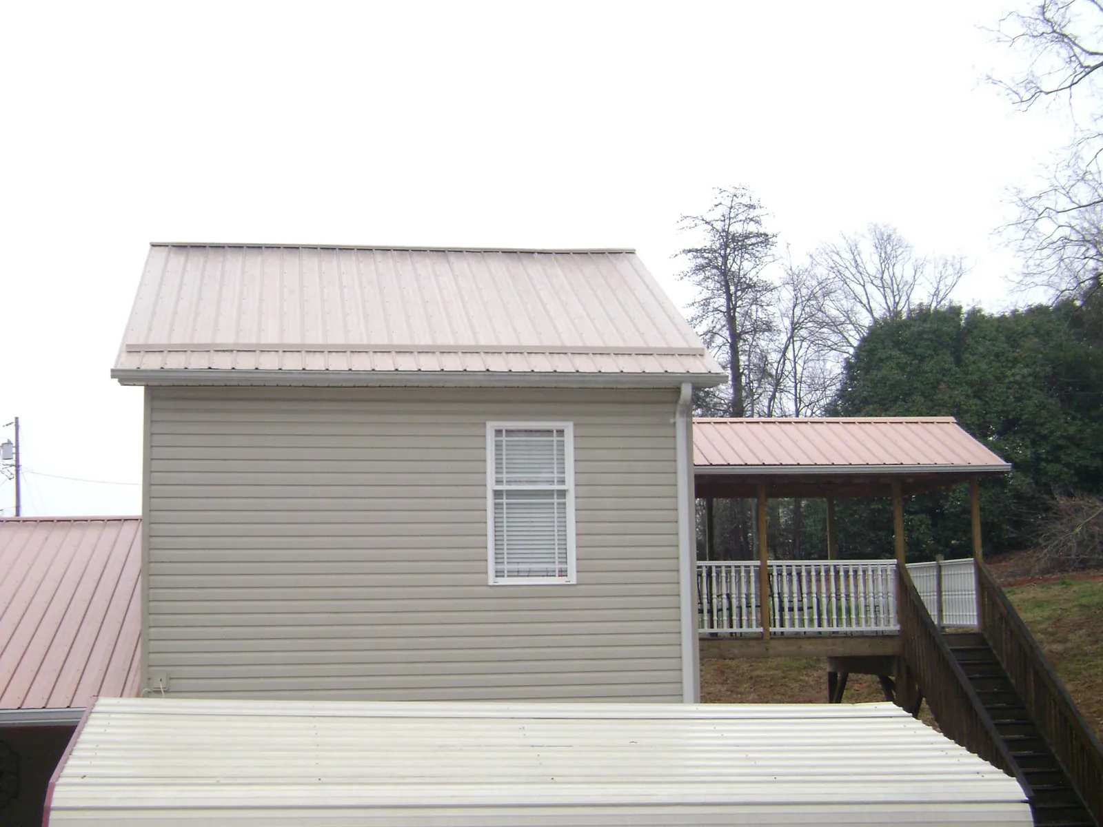 Tan metal roofs on a two story addition and attached porch, from a Roof Replacement job in Okolona